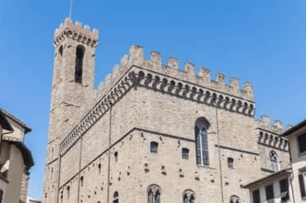 A stone mediaeval building with crenellated walls and a tall square tower is shown against a clear blue sky.
