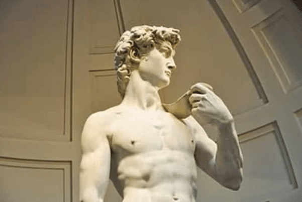 Marble statue of a nude male figure with curly hair, holding an object over his left shoulder, displayed under a domed ceiling.