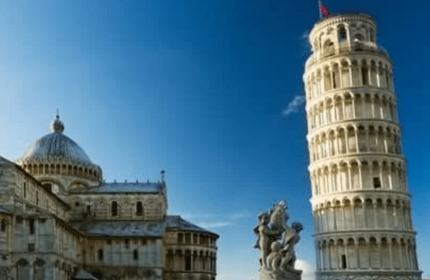 The Leaning Tower of Pisa, a freestanding bell tower, stands beside a cathedral under a clear blue sky with a statue in the foreground.