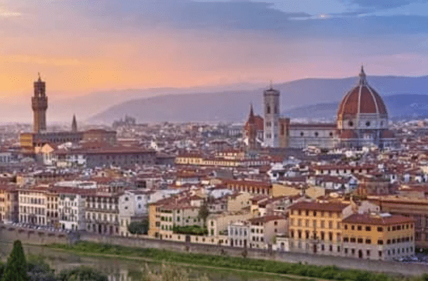 Panoramic view of Florence at sunset, featuring the Florence Cathedral dome and historical buildings under a colourful sky.