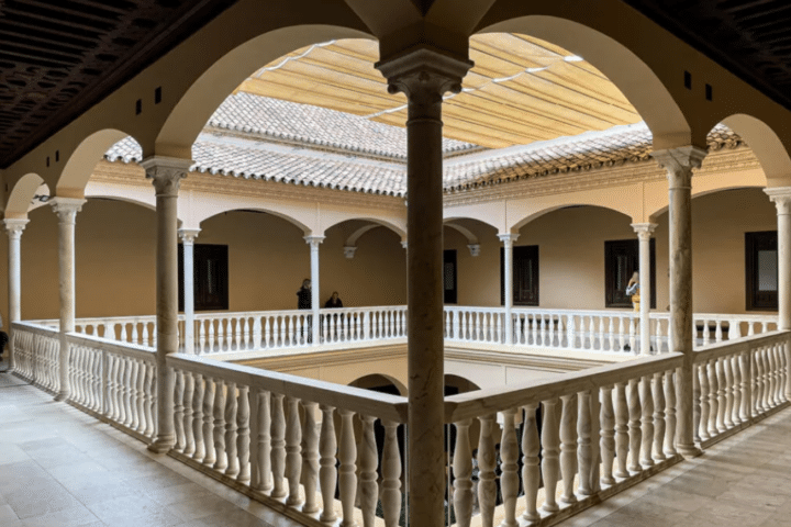 Open-air courtyard with marble columns and arches, surrounded by a covered walkway and tiled roof; a few people stand by the walls in the background.