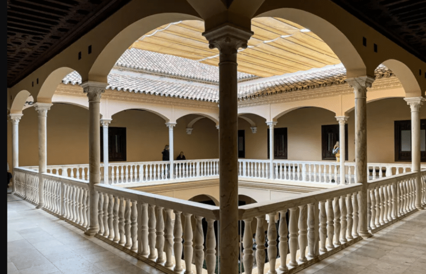 Open-air courtyard with marble columns and arches, surrounded by a covered walkway and tiled roof; a few people stand by the walls in the background.