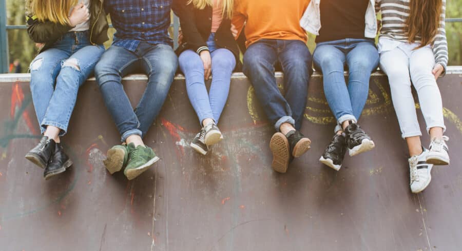 Six people sitting in a row on the edge of a graffiti-covered SEND skate ramp.
