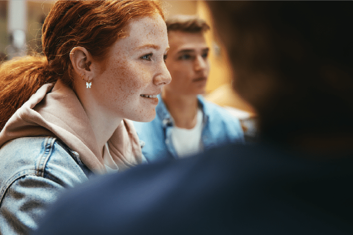 A young woman with red hair and freckles listens during a SEND group discussion.